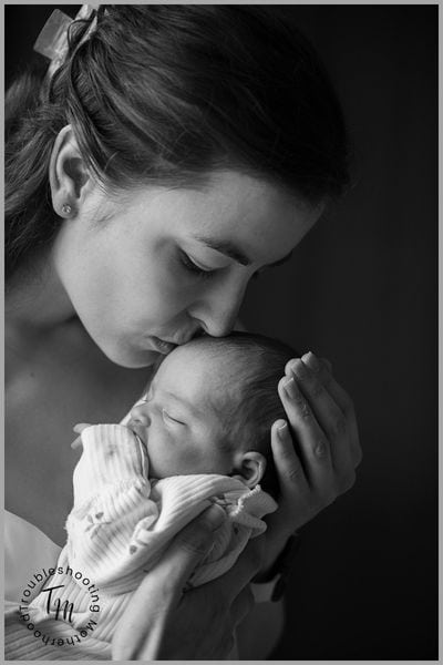 Postpartum must haves for new moms. Image of mom kissing newborn in head.