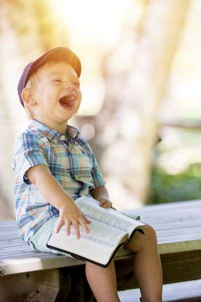 boy laughing while reading book. Best fairy tales to read to little kids.