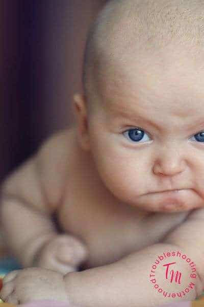 A close-up of a baby with a stern expression, lying on a colorful surface, emphasizing the contrast between their innocence and a tough demeanor, suitable for themes like badass boy names or strong male characters.