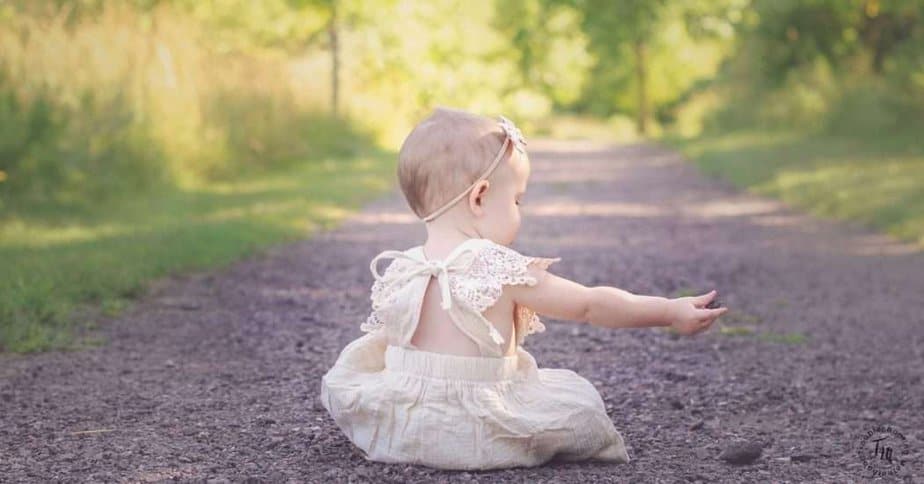 Pretty baby Girl names. Image of teh back of a little girl sitting on a pathway, wearing a cream colored dress. 