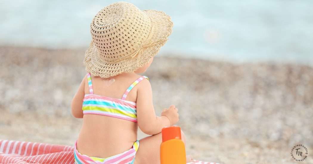 Baby Girl sitting on the beach, back to the camera, in a bikini, with a hat on, looking at the ocean. Beachy Girl Names. 