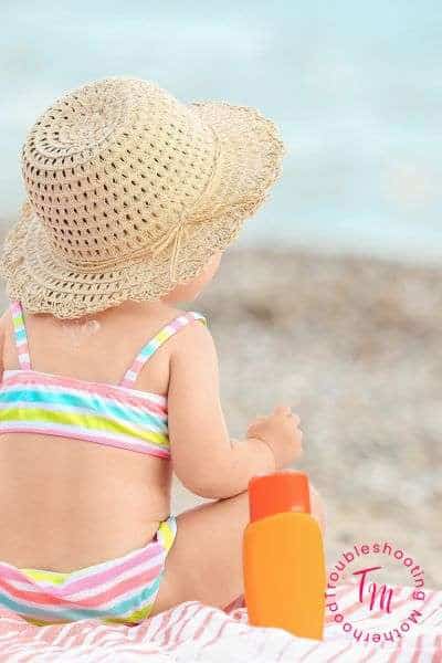 Baby girl in a colorful swimsuit and sun hat sitting on a beach, perfect for a post about beachy girl names, cute sea names, and tropical summer-inspired baby name ideas.