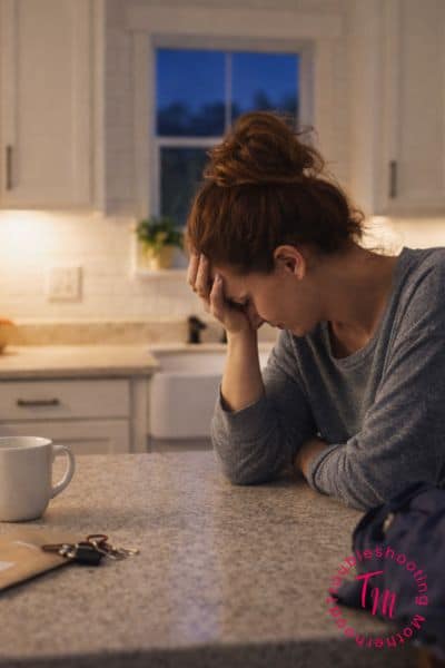 A tired woman in a bright kitchen at night, representing how to clean when you’re mentally exhausted without doing too much.